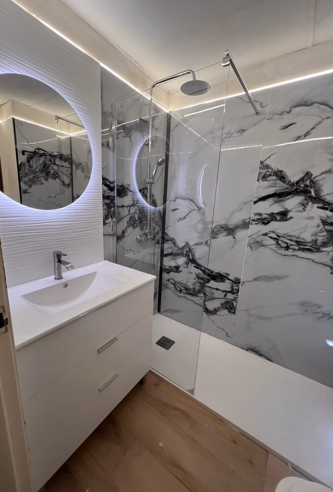 Baño en mármol blanco veteado con ducha, espejo circular retroiluminado y mueble suspendido