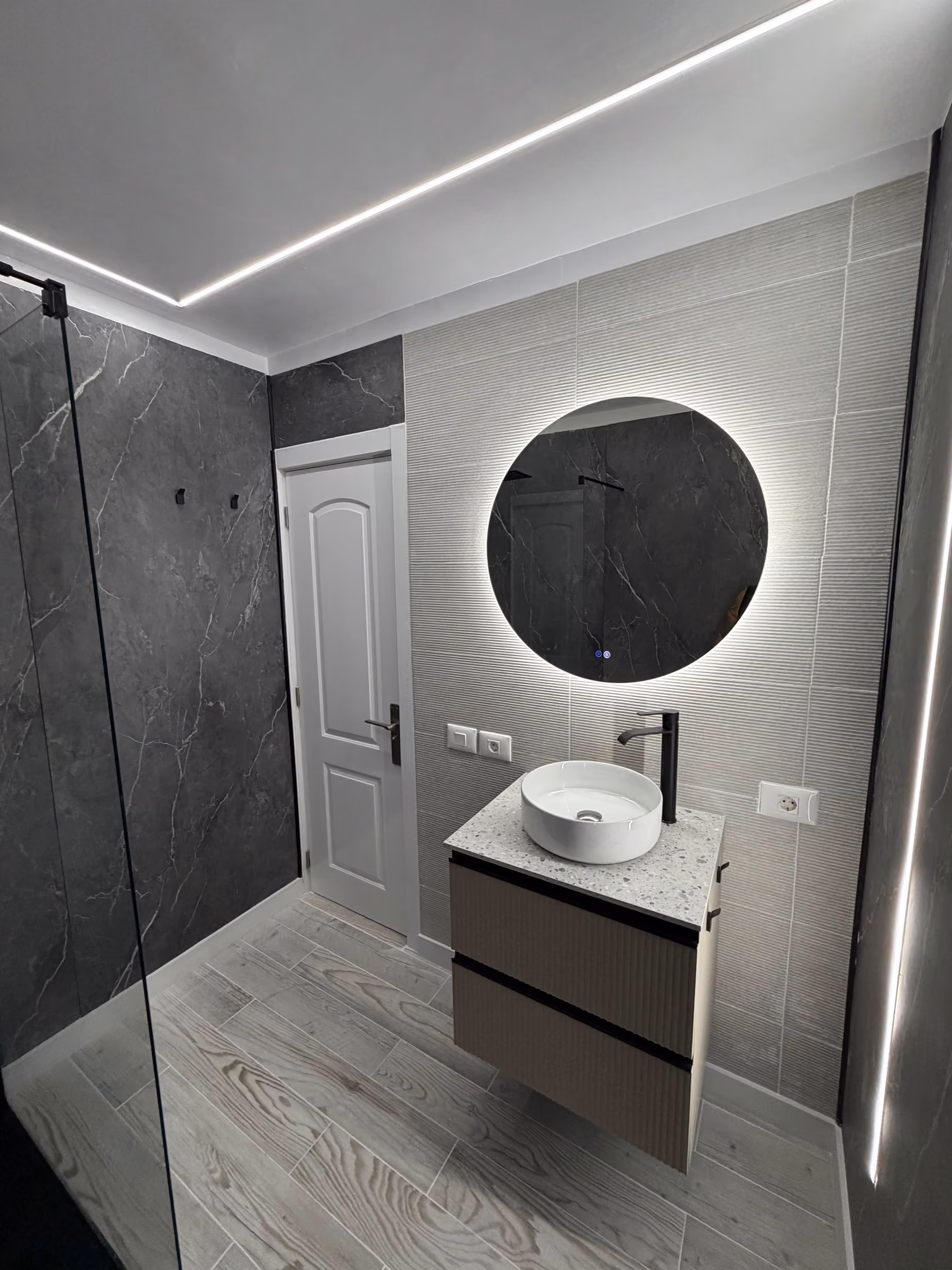 Lavabo circular bajo espejo redondo retroiluminado sobre encimera de mármol