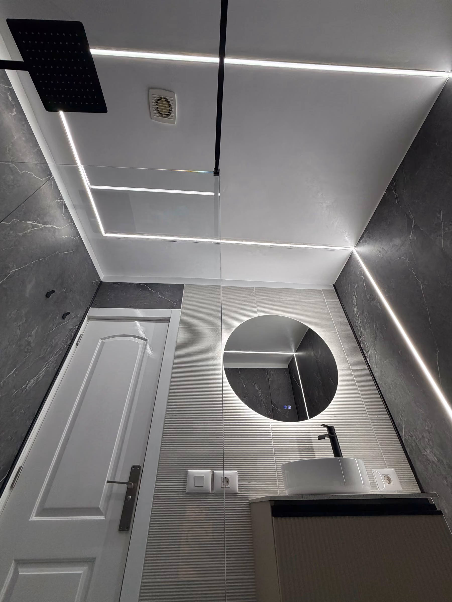 Vista general del baño con lavabo, espejo circular y perfiles de luz LED