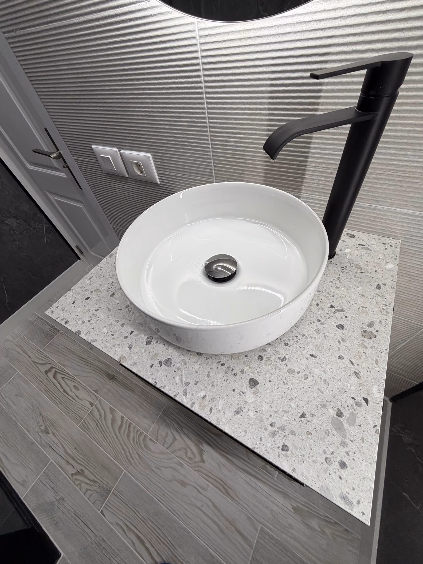 Detalle de lavabo circular sobre encimera de terrazo con grifería negra mate