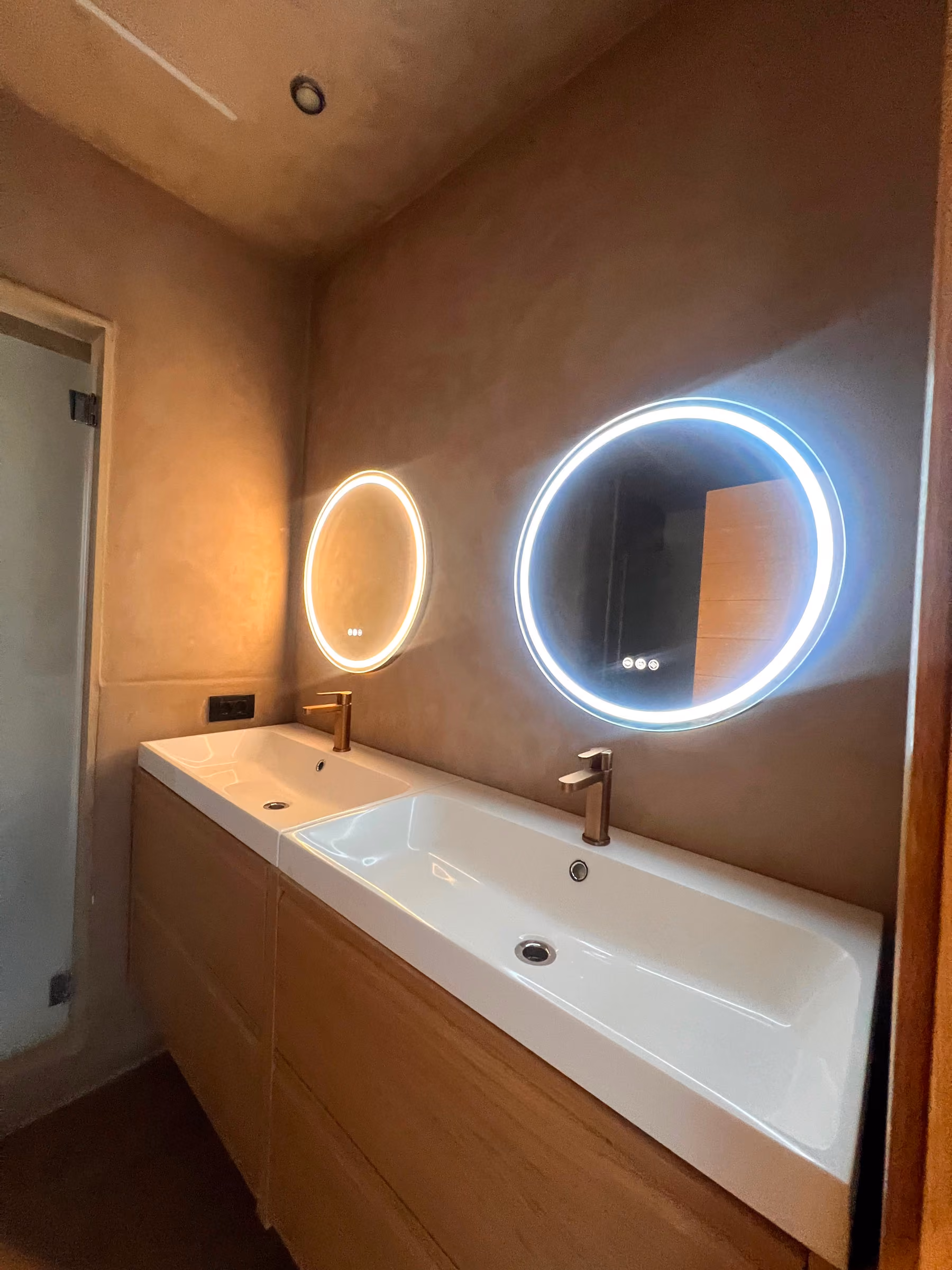 Detalle de los dos lavabos y espejos circulares retroiluminados en tonos cálidos y fríos