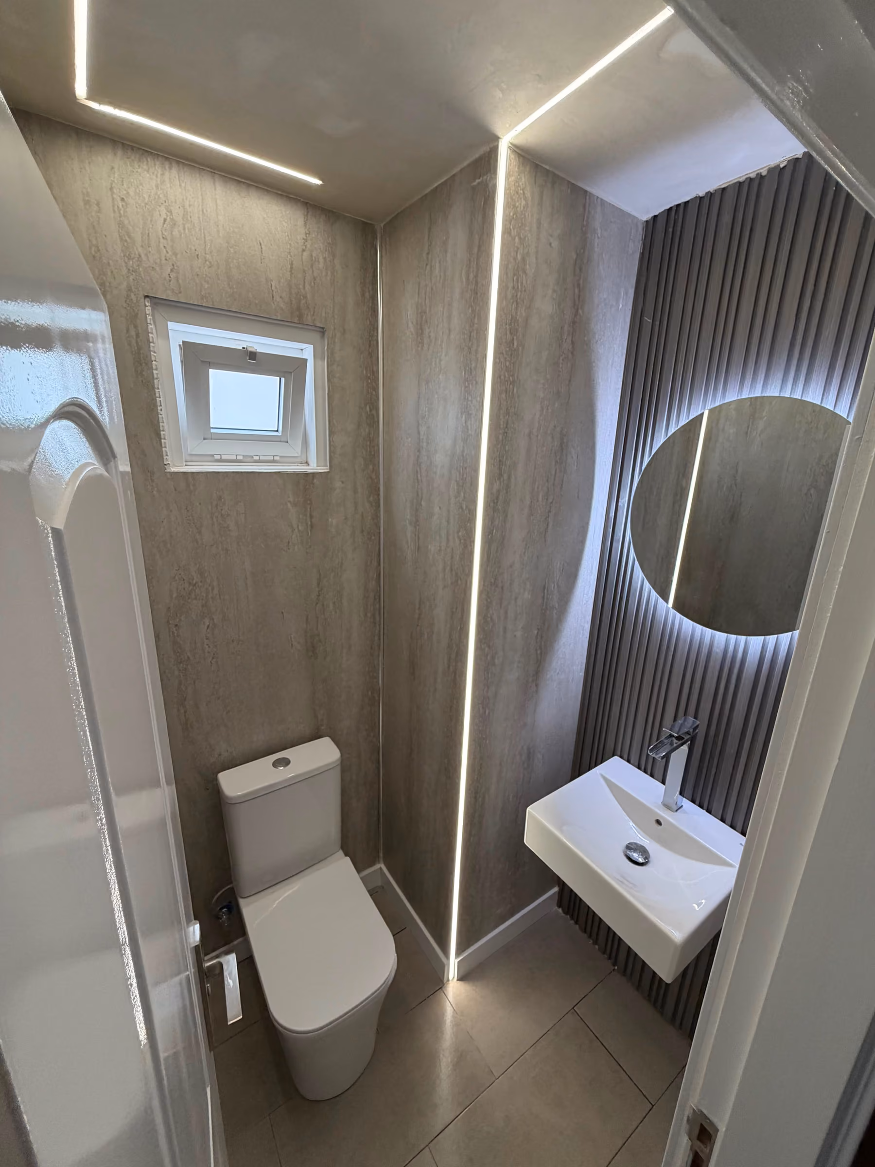 Aseo en travertino con inodoro y lavabo bajo espejo circular retroiluminado