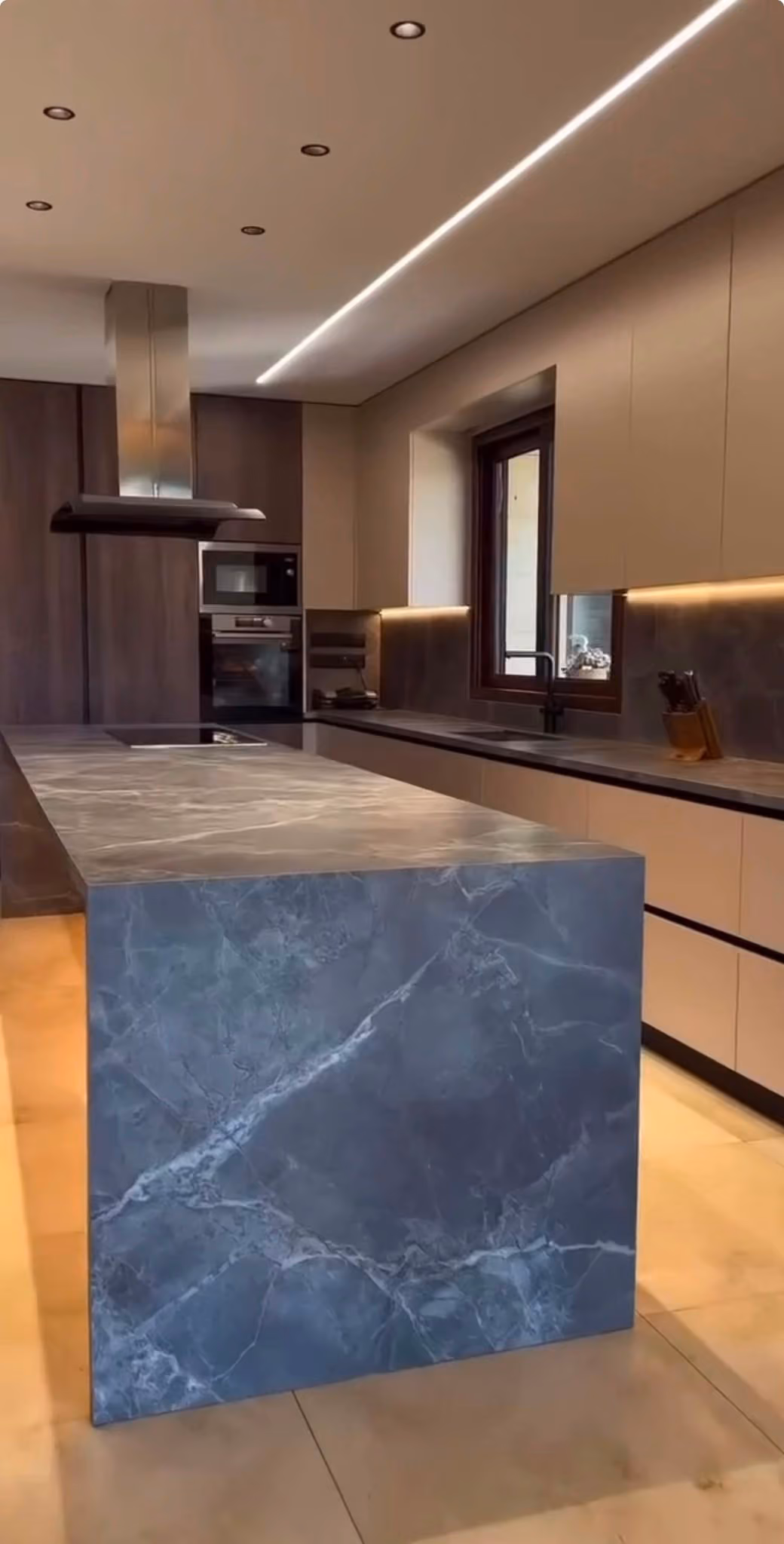 Vista general de la cocina en madera oscura con isla en mármol azulado y placa de inducción