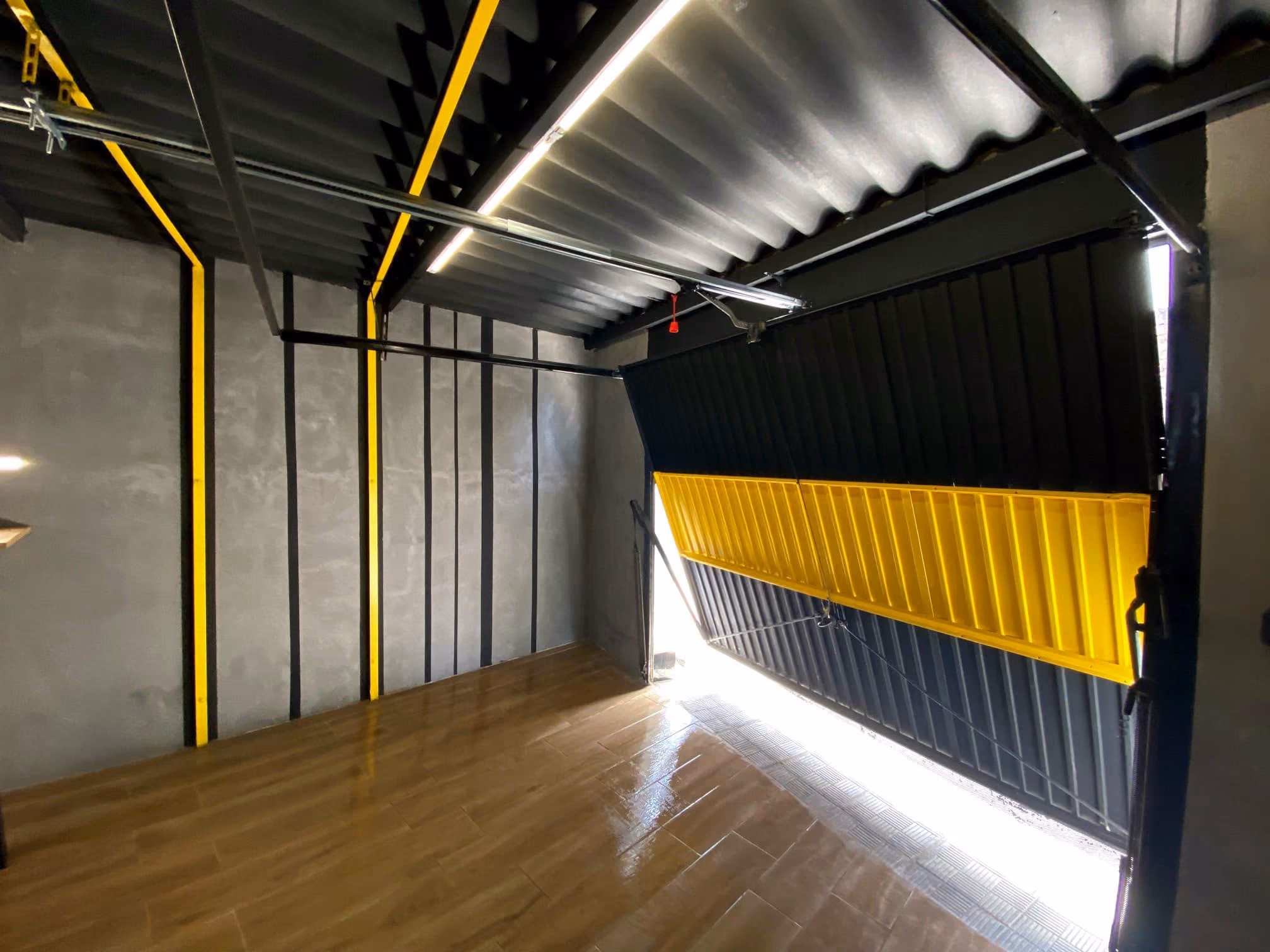 Vista del garaje hacia la puerta seccional abierta, con estructura metálica y detalles en amarillo