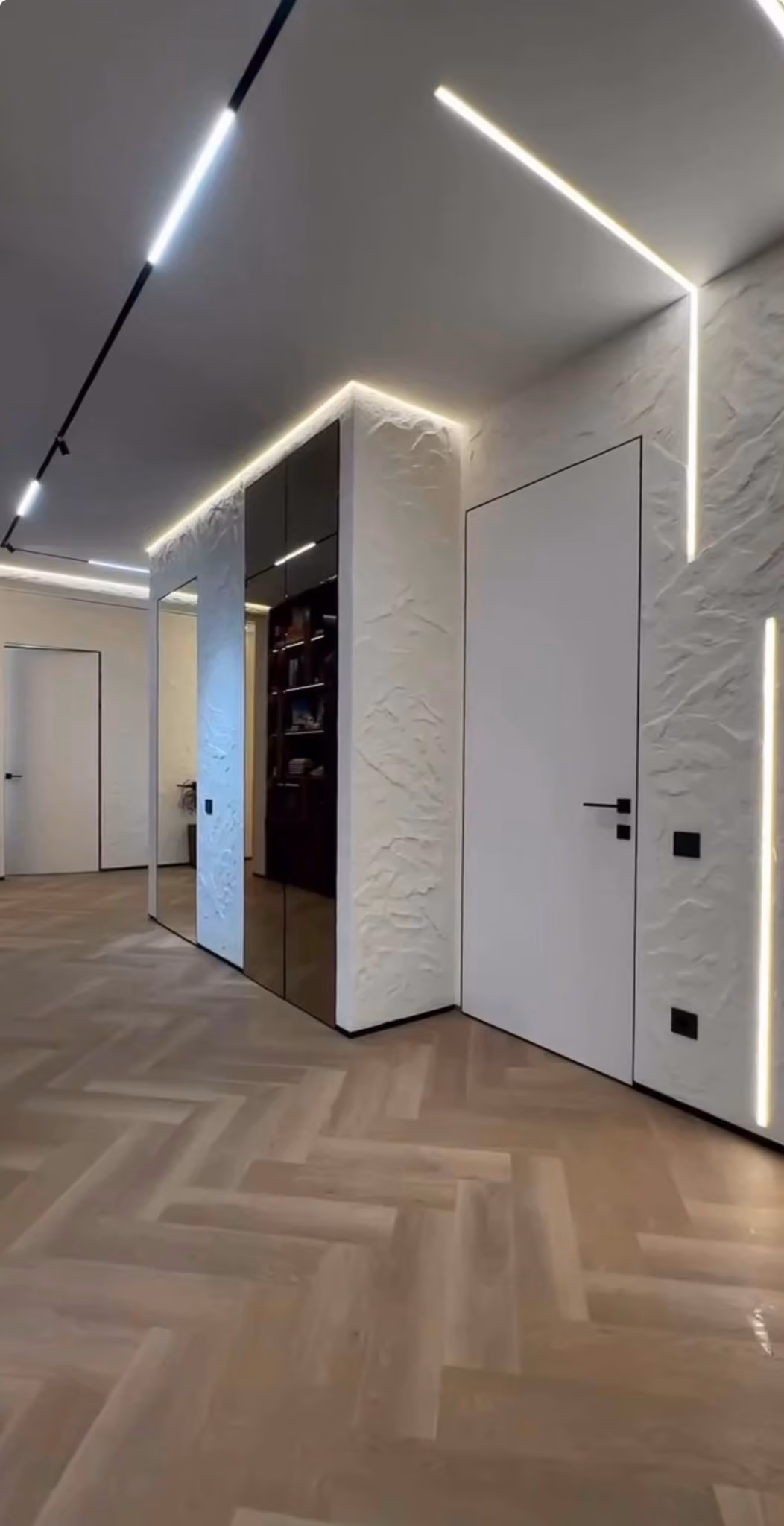 Vista del pasillo con estantería empotrada, puertas en blanco y perfiles de luz LED cruzados en el techo