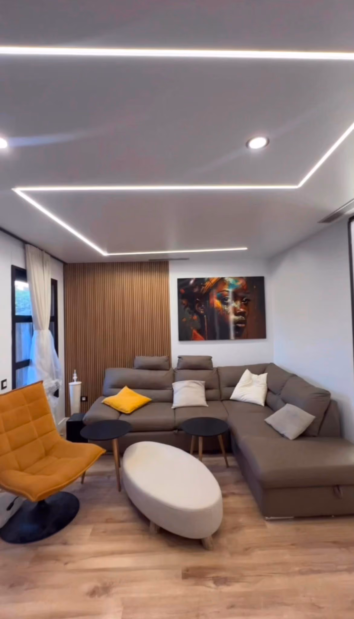 Salón con sofá rinconero, sillón mostaza y panel de librillo de madera