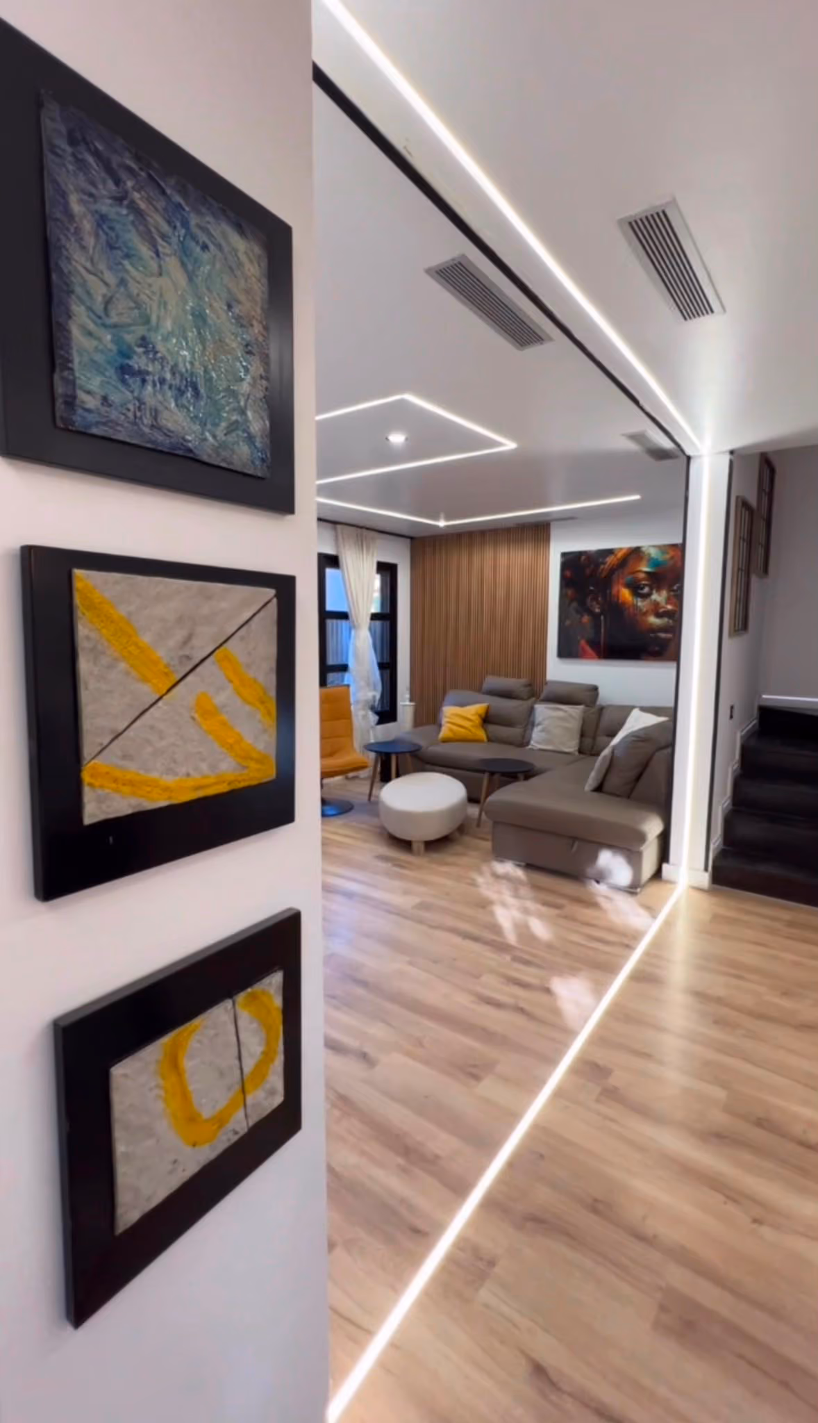 Vista del salón desde el pasillo, con cuadros abstractos en primer plano y sofá rinconero al fondo