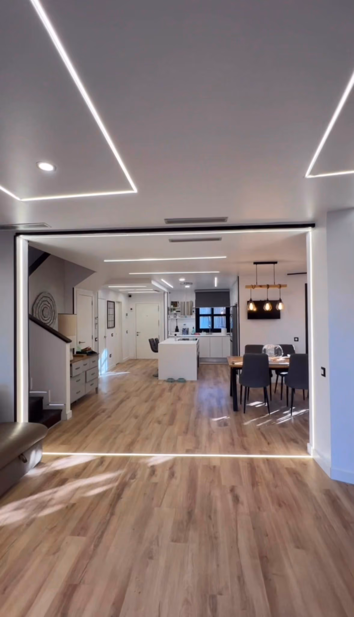 Vista del mismo salón hacia la cocina abierta, con isla, mesa de comedor y lámparas colgantes de madera
